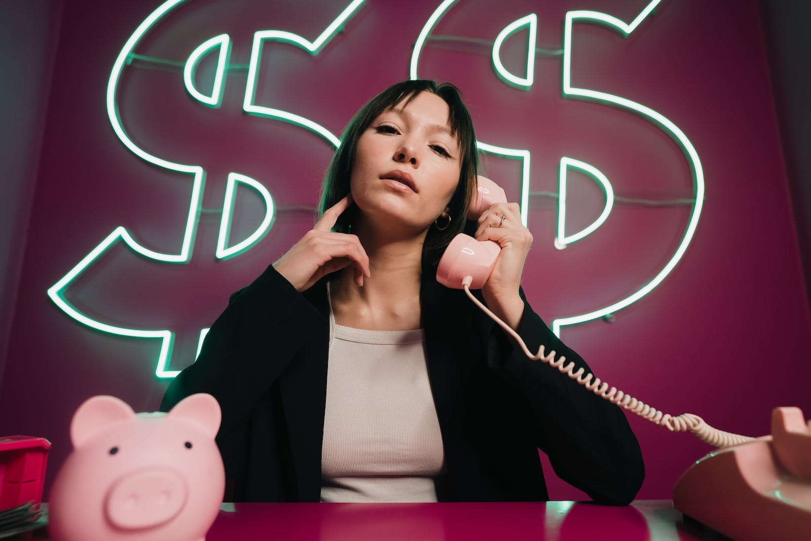 A woman sitting at a desk with a pink piggy bank and a sign that says dollar